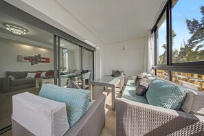 Un saló modern amb un sofà, una porta de vidre que dona a un balcó i una zona de menjador amb una taula i cadires.