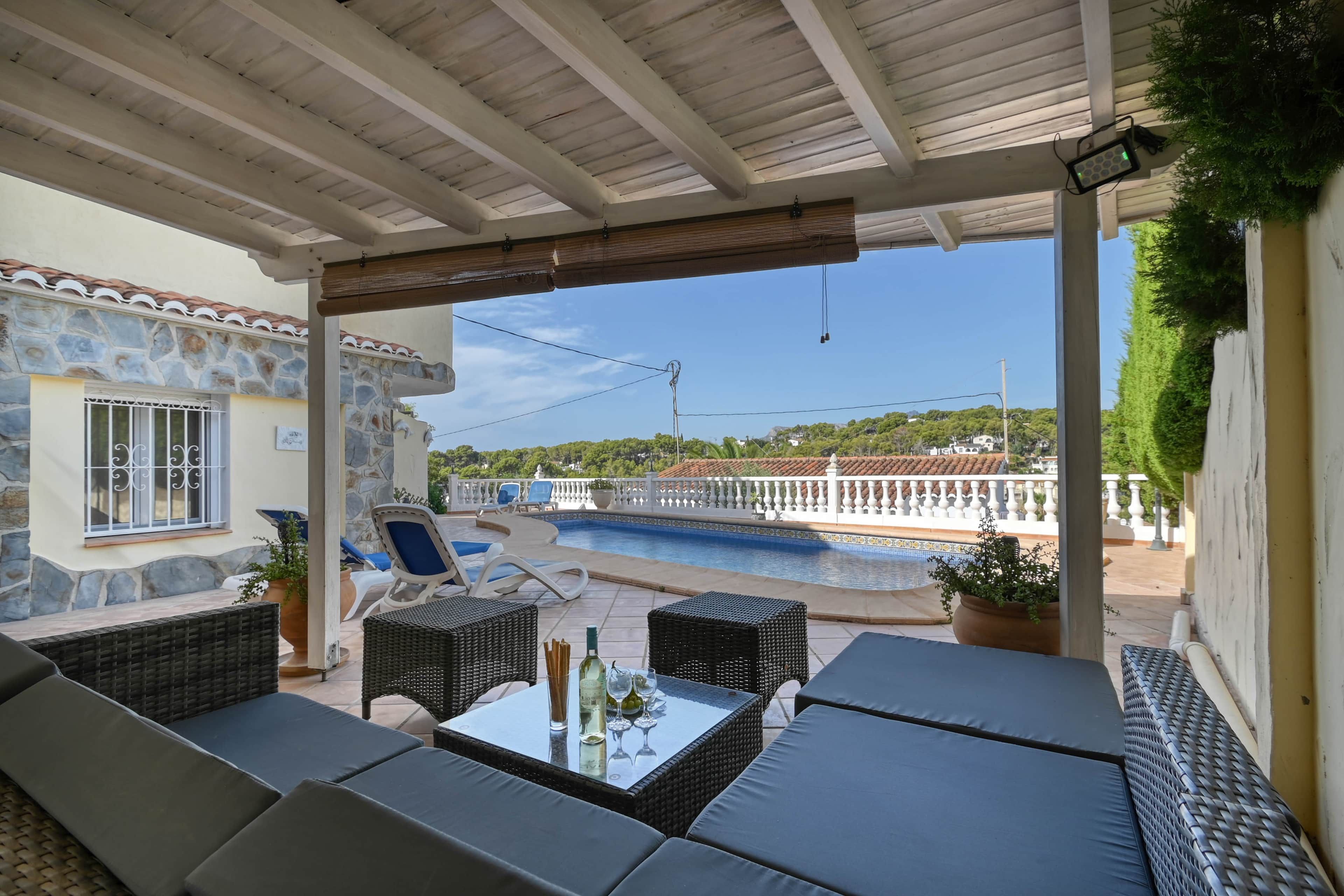 Ein überdachter Außenbereich mit Korbmöbeln und Blick auf einen Swimmingpool.