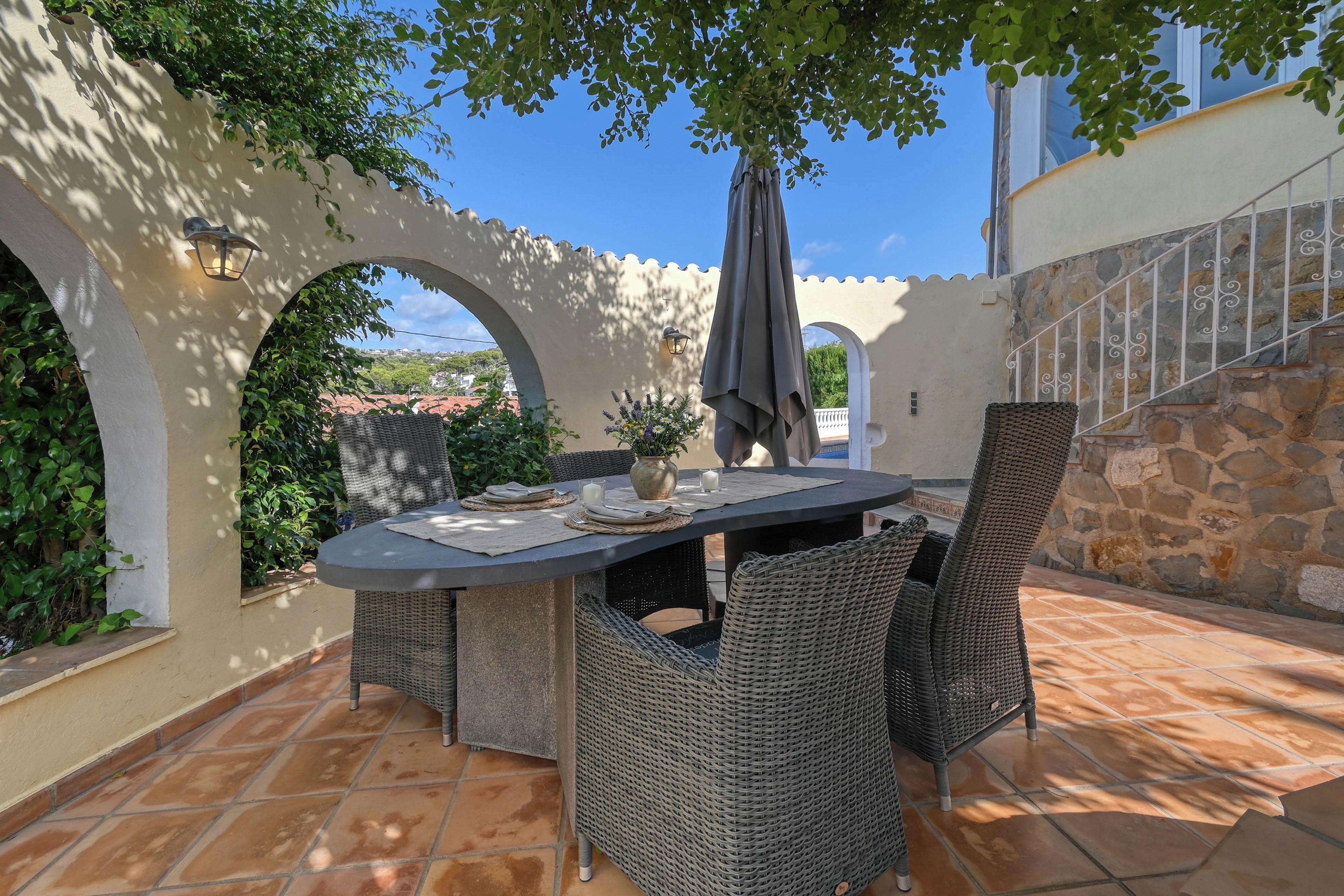 An outdoor patio with a round table, wicker chairs, and an umbrella.