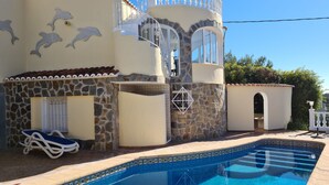 Una casa con piscina, paredes de piedra y un balcón con barandilla blanca.