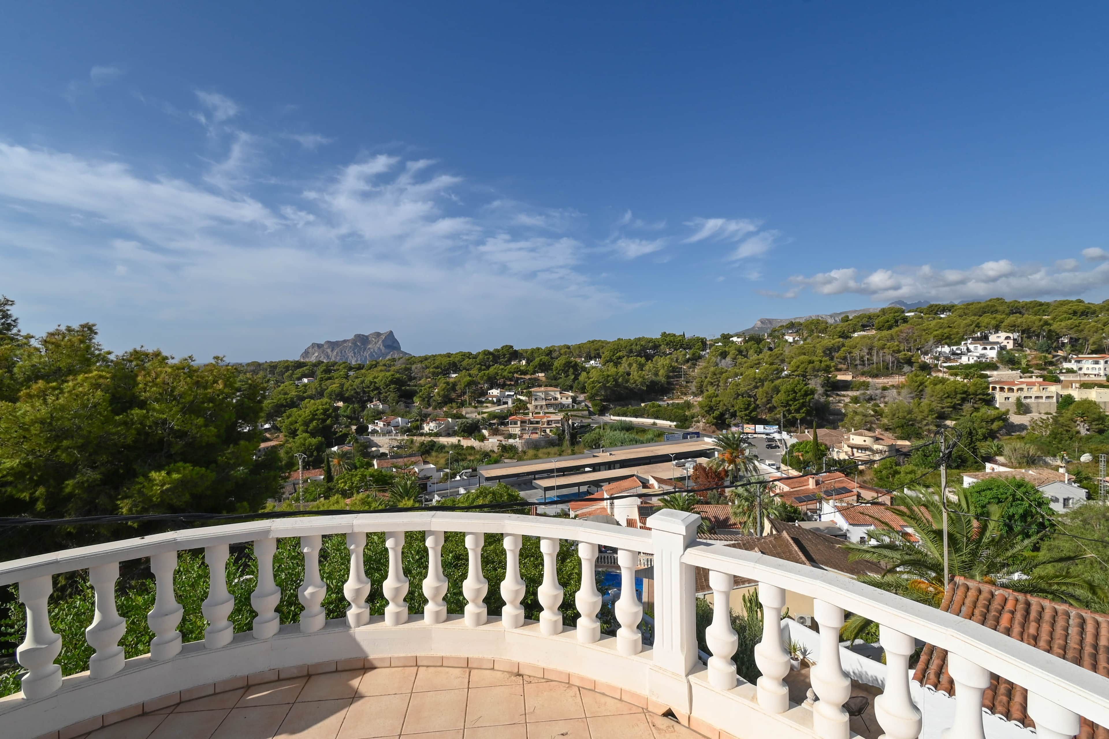 A balcony with a white balustrade overlooking a residential area with houses and a mountain in the distance.