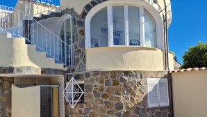 Un edificio de varios pisos con fachada de piedra, un balcón con barandillas blancas y una entrada con tejas.