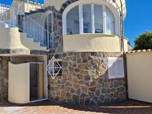 Un edificio de varios pisos con fachada de piedra, un balcón con barandillas blancas y una entrada con tejas.