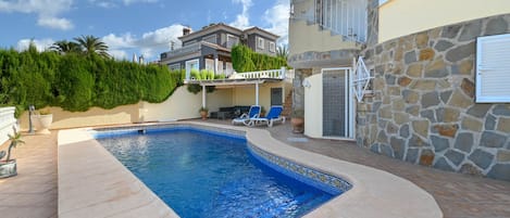 A swimming pool with a tiled edge, a stone wall, and a door with a metal gate.