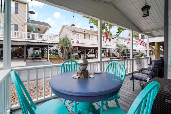 A covered outdoor seating area with turquoise chairs and a round table, overlooking a street with buildings and parked cars. - Ocean Lakes Family Beach Resort & Waterpark (Myrtle Beach)