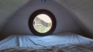 A bedroom with a circular window, wooden ceiling, and a bed with white bedding.