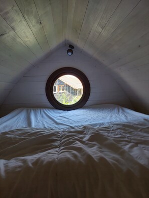 A bedroom with a circular window, wooden ceiling, and a bed with white bedding. - Vrbo Property (saint julien de lampon)