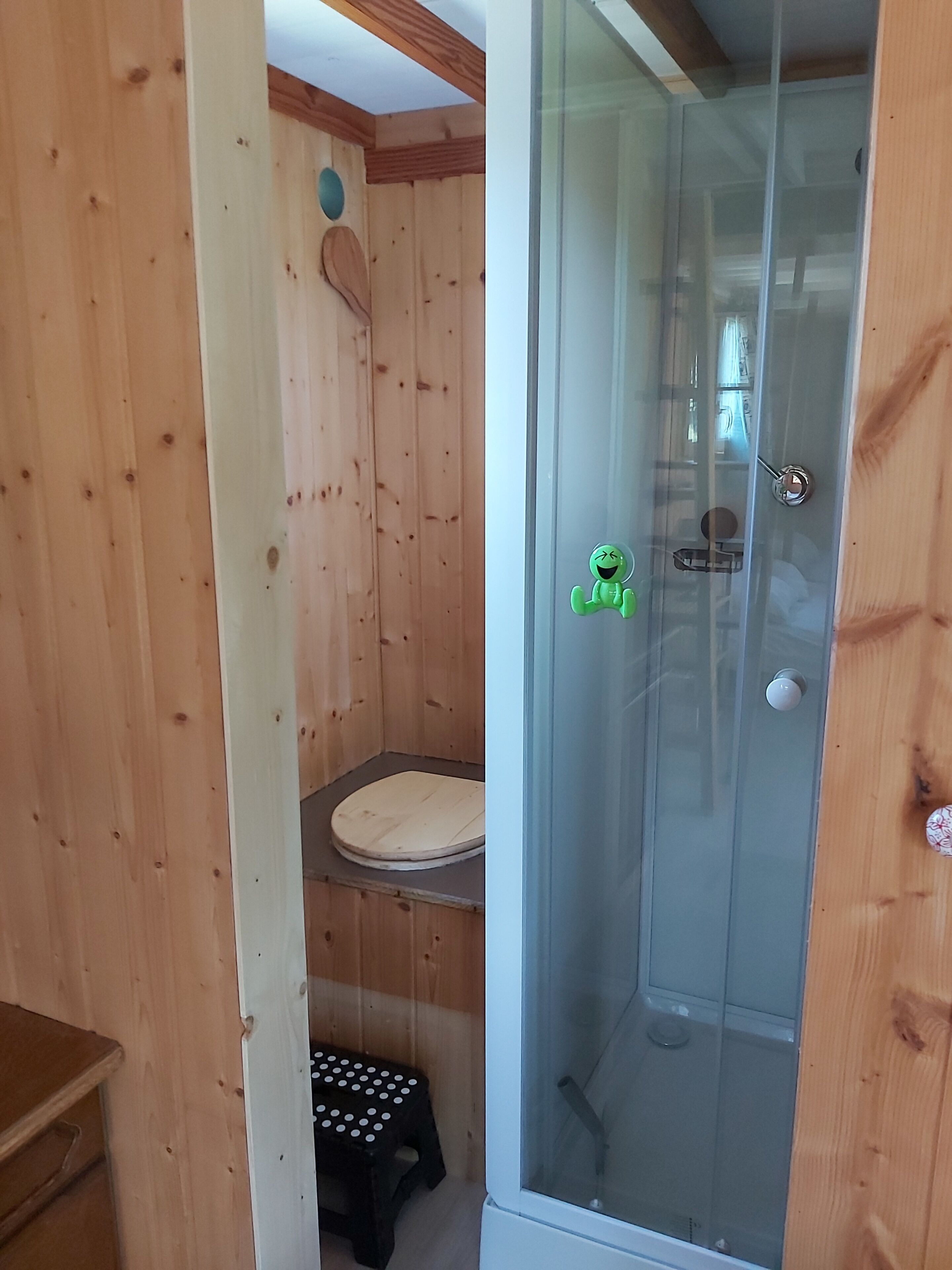 Ambiente interno in legno con doccia vetrata, un water e uno sgabello.