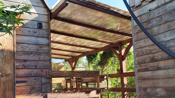 A wooden structure with a covered patio area, a bench, and a small table.