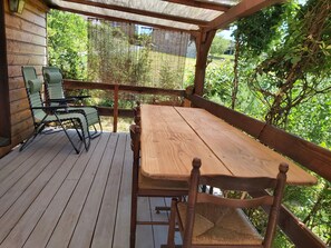 A wooden deck with a table and chairs, surrounded by greenery. - Vrbo Property (saint julien de lampon)