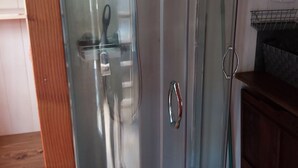 A glass-enclosed shower with a stainless steel handle, a wooden floor, and a metal rack on the wall.