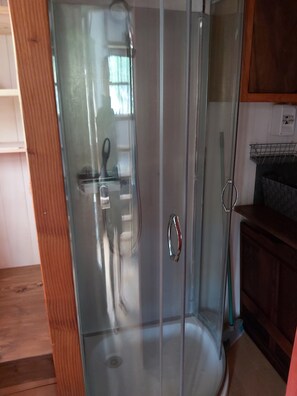 A glass-enclosed shower with a stainless steel handle, a wooden floor, and a metal rack on the wall. - Vrbo Property (saint julien de lampon)