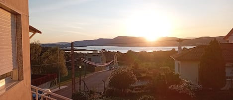 A residential area with a view of the sunset over a body of water, a street, and some greenery.