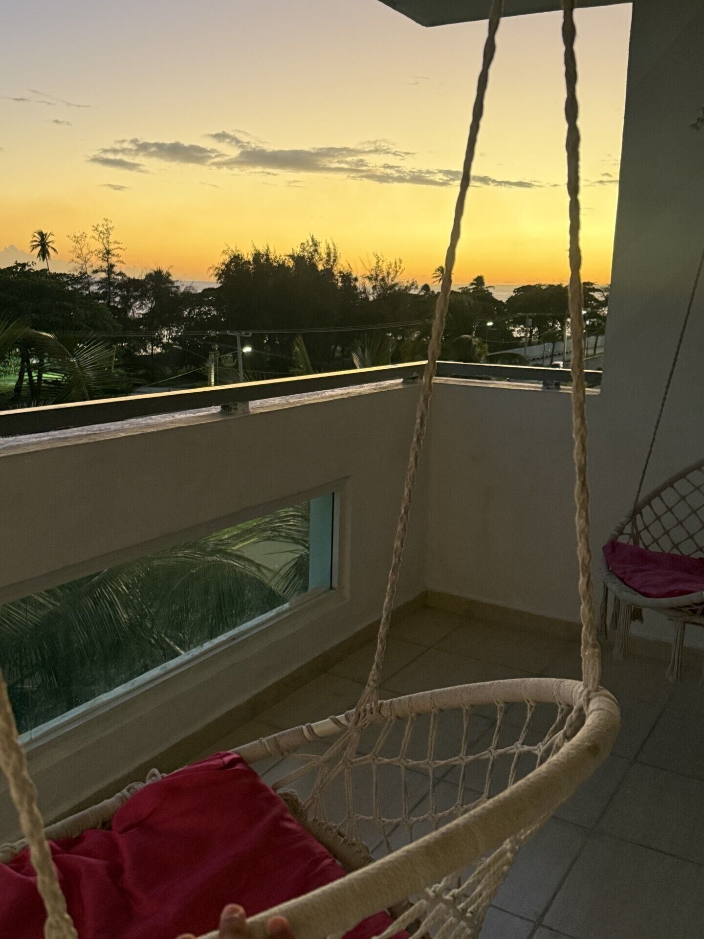 Un balcon avec un fauteuil suspendu, une fenêtre et une vue sur le coucher de soleil.