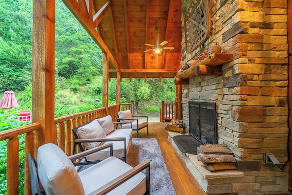 Un espacio de estar al aire libre techado con chimenea de piedra, terraza de madera y vistas a un paisaje verde exuberante.