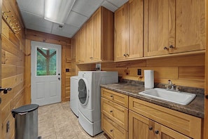 A compact kitchen with wooden cabinets, a washing machine, a sink, and a trash can.