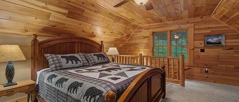 Quarto de cabana de madeira com uma cama, um ventilador de teto, uma janela e um abajur.