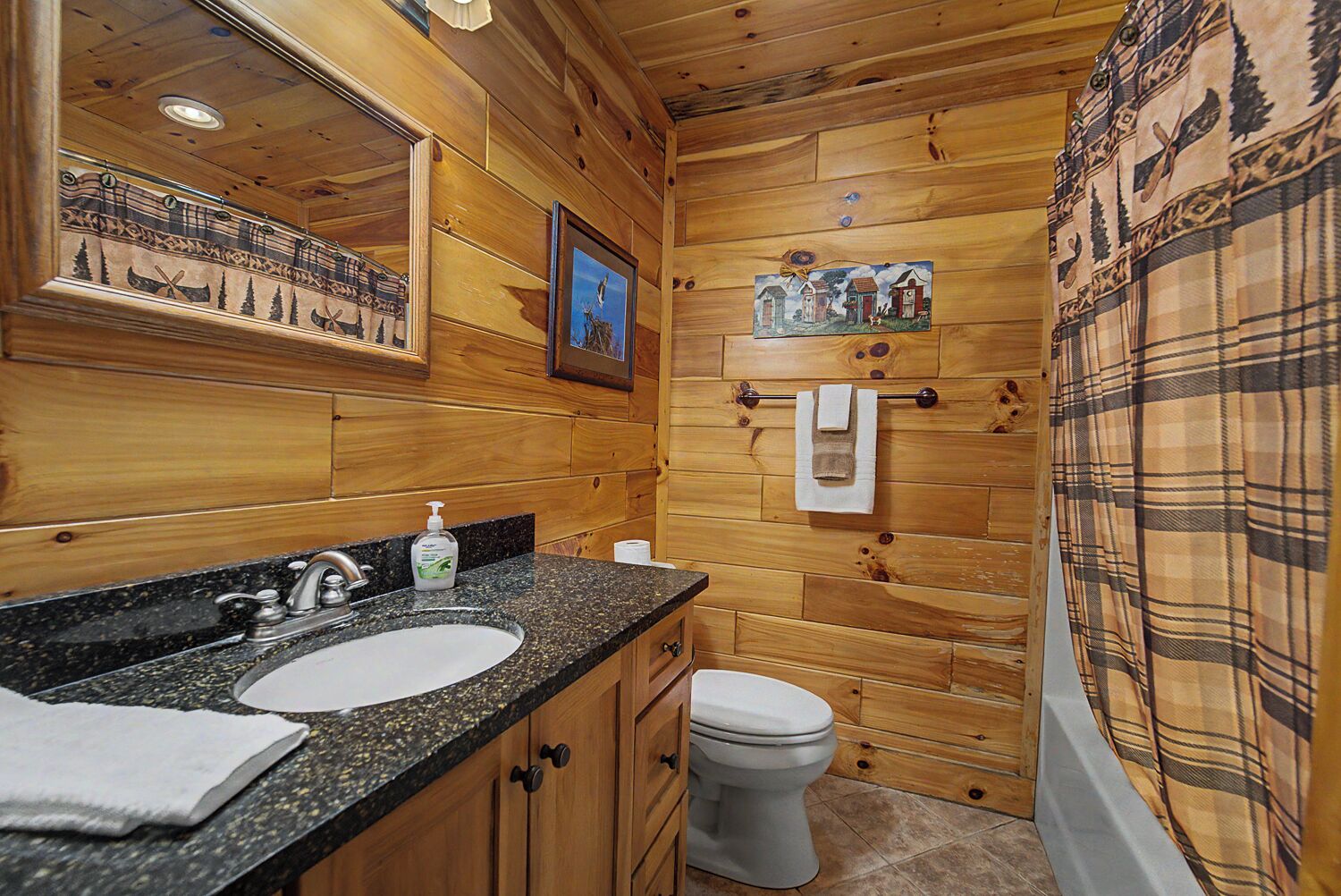 A wooden cabin-style bathroom with a granite countertop sink, a toilet, and a shower curtain with a forest pattern.