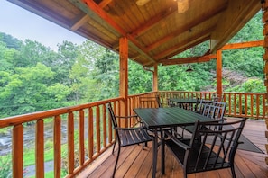 An outdoor deck with a table and chairs, surrounded by a wooden railing, overlooking a forested area.