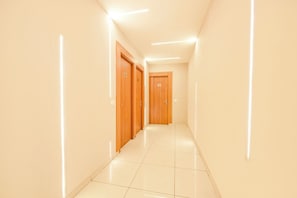 A corridor with wooden doors, white walls, and a tiled floor. - Hotel DC Prime (Zirakpur)