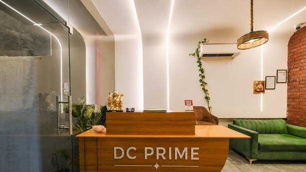 A reception desk labeled 'DC PRIME' with a modern design, a green sofa, and a hanging light fixture.