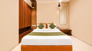 A modern hotel room with a large bed, wooden wardrobe, a mirror, and a nightstand with a lamp.