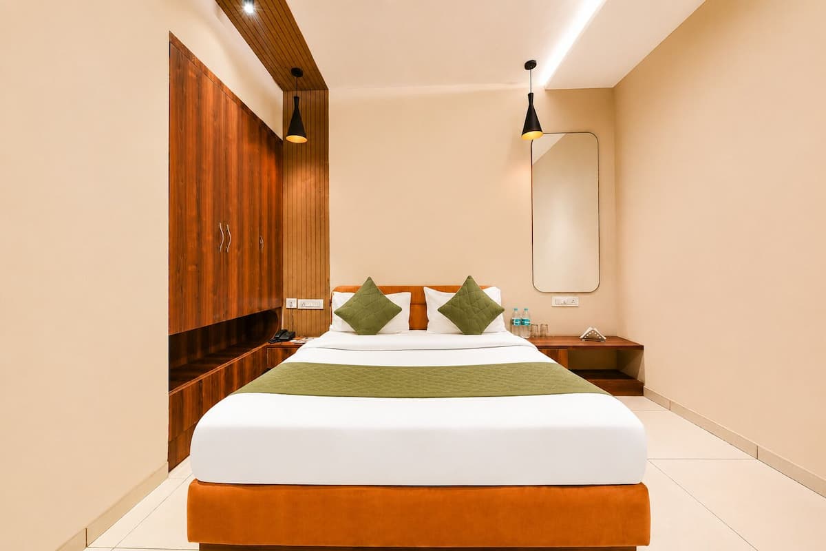 Una habitación de hotel moderna con una cama grande, un armario de madera, un espejo y una mesita de noche con lámpara.