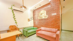A reception area with a brick wall, a green and a pink sofa, a wooden desk, and a hanging plant.