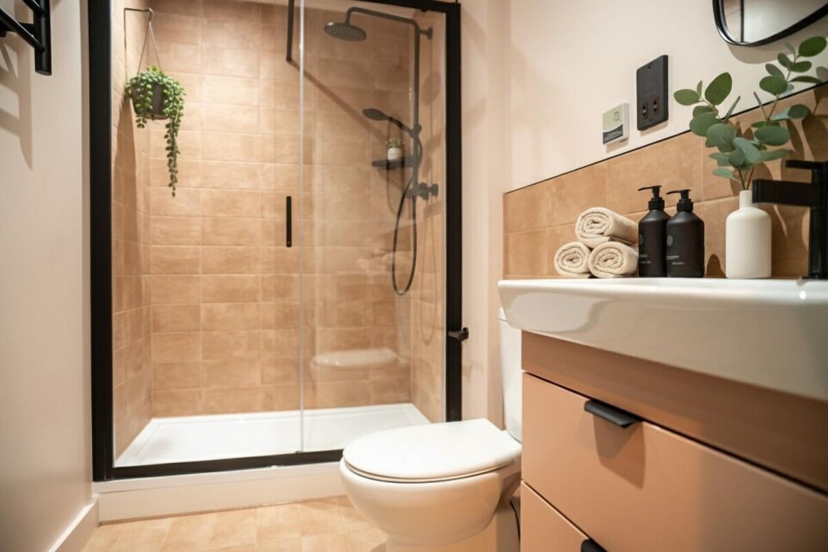 A bathroom with a glass-enclosed shower, a toilet, and a vanity with toiletries.