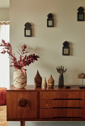 A wooden dresser with a vase of red leaves, decorative pottery, and wall-mounted mirrors. - Southall &Soul (Hayes)