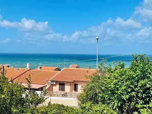 Ein Küstenwohngebiet mit Häusern mit Terrakotta-Dächern, blauem Himmel und dem Meer im Hintergrund.