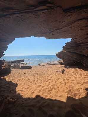 Vista de una playa a través de un arco natural de roca, con cielo azul despejado y mar tranquilo.