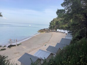 A beach with a row of small, white, single-story buildings with metal roofs, a sandy beach, and calm water. - Rent house Noirmoutier, close to bois de la chaize and the sea 10 beds (Noirmoutier-en-l'Île)