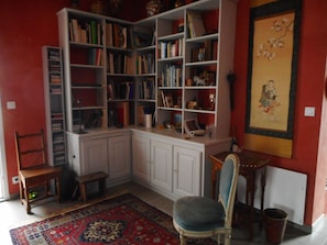 Ein Eckzimmer mit Bücherregal, einem Sessel, einem Teppich und einem Bild an der Wand.