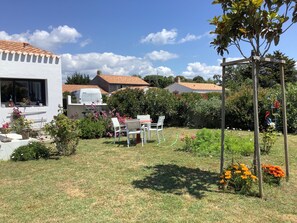 Ein Garten mit einem weißen Gebäude, einem Essbereich mit Stühlen und einer Pergola.