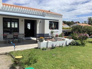 Ein modernes Haus mit überdachter Veranda, Sitzgelegenheit im Freien und einem Garten.