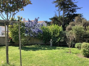 Ein Garten mit einer Pergola, verschiedenen Sträuchern und einer Statue.