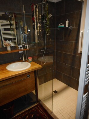 Ein Badezimmer mit einer gläsernen Duschkabine, einem Holzkosmetikschrank und einem Spiegel.