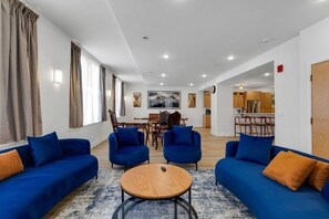 A modern living room with blue sofas, a round coffee table, and a dining area with wooden furniture.