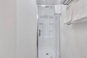 Eine schmale, geschlossene Duschkabine mit Tür, einem Handtuchhalter an der Wand und einem sichtbaren Bedienfeld.