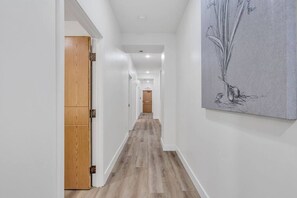 A hallway with wooden flooring, white walls, and a door on the left.