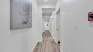 A hallway with a wooden floor, white walls, and a fire alarm sign. - Downtown Indy-Entire Building-77 Guests (Indianapolis)