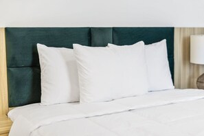 A neatly made bed with white bedding and pillows, a dark green upholstered headboard, and a wooden nightstand with a lamp. - Downtown Indy-Entire Building-77 Guests (Indianapolis)