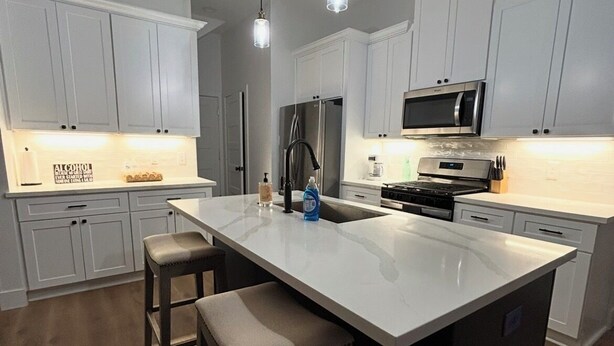 A modern kitchen with white cabinets, a large island with stools, stainless steel appliances, and pendant lighting. - Conveniently located Spacious Houston Heights Home-King Suite-Sleeps 6 (Houston)