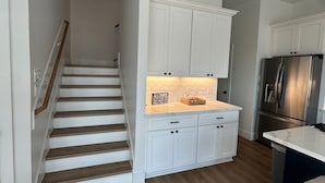 A kitchen with white cabinets, a stainless steel refrigerator, and a wooden staircase. - Conveniently located Spacious Houston Heights Home-King Suite-Sleeps 6 (Houston)