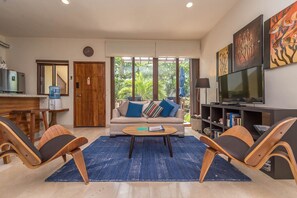 Ein modernes Wohnzimmer mit einer Couch, einem Couchtisch, zwei Sesseln, einem Fernseher und Kunstwerken an der Wand.