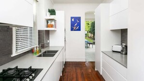 Una cucina angusta con mobili bianchi, un piano cottura nero e un'opera d'arte blu appesa al muro.