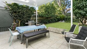 Patio esterno con tavolo, sedie e barbecue.