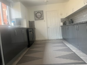 A kitchen with dark cabinets, a dishwasher, a clock on the wall, and a patterned rug.