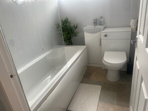 A bathroom with a bathtub, toilet, sink, and a potted plant. - Central Sutton on Sea 4-bed House, Sleeps 8 (Mablethorpe)